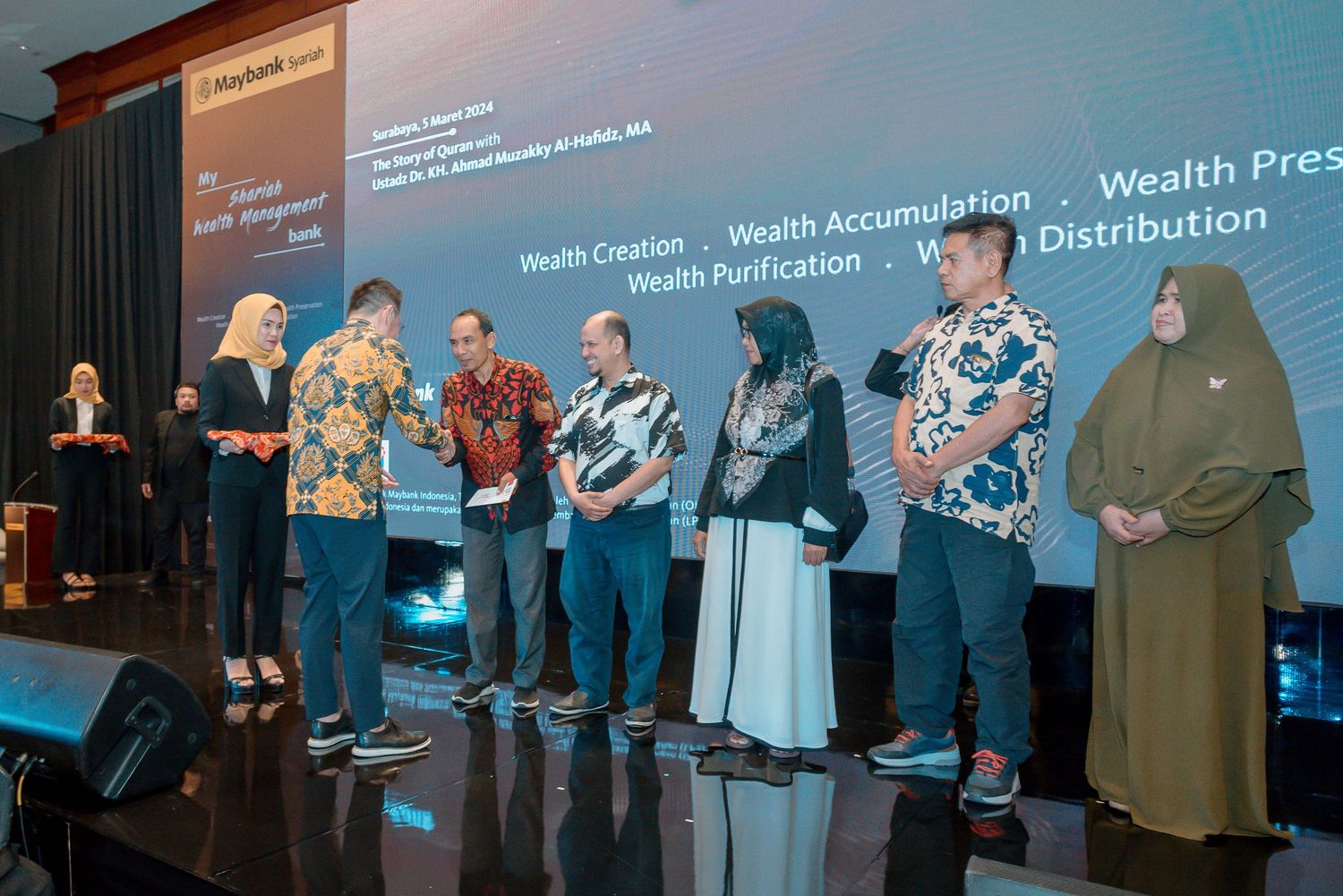 A group of people standing on a stage with a blue illuminated backdrop during an event presentation.