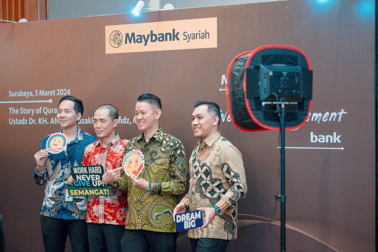 Group wearing colorful batik shirts pose together at Maybank Syariah corporate event.