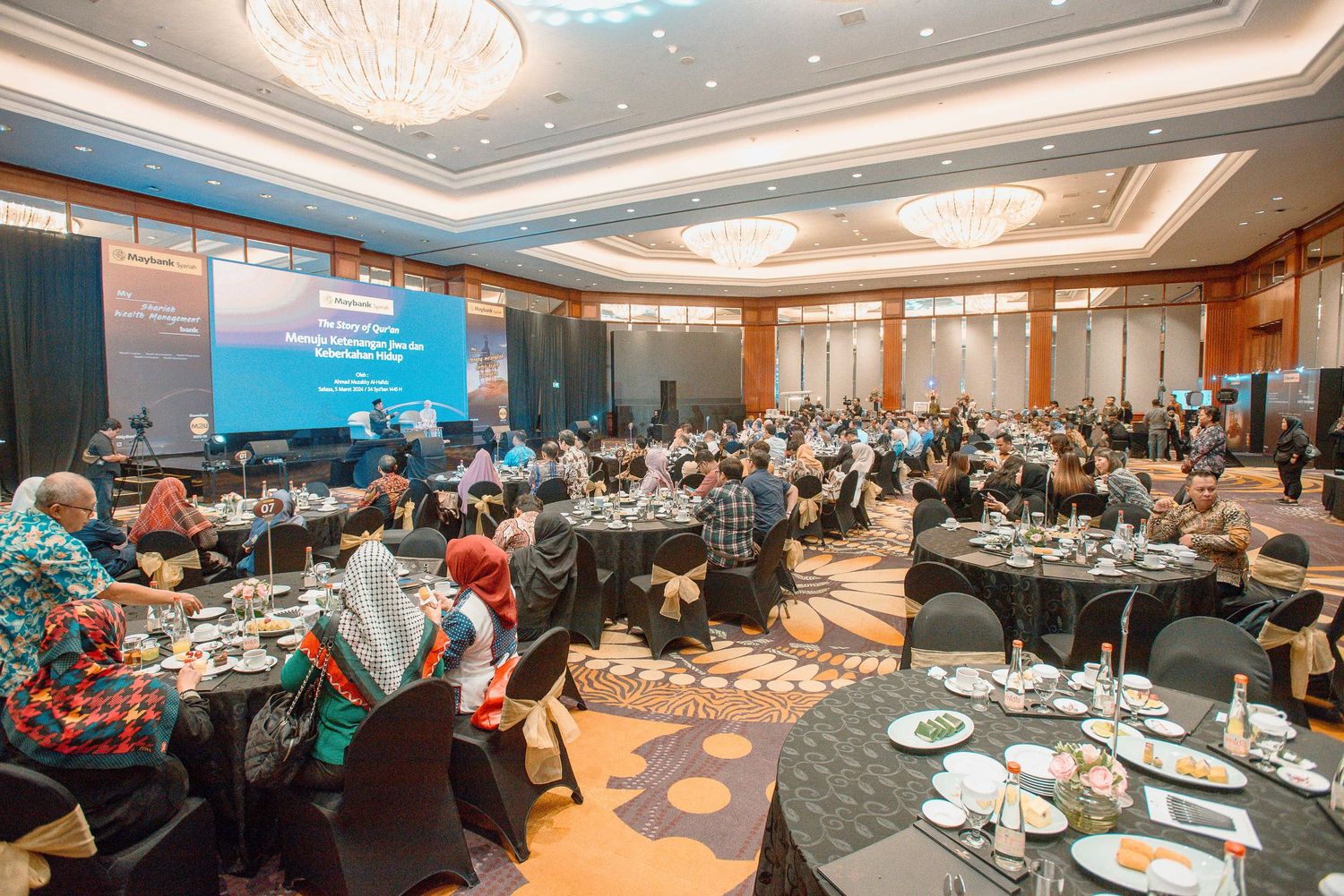 Elegant banquet hall setup with round tables, formal place settings, and ornate chandeliers in a modern conference venue.