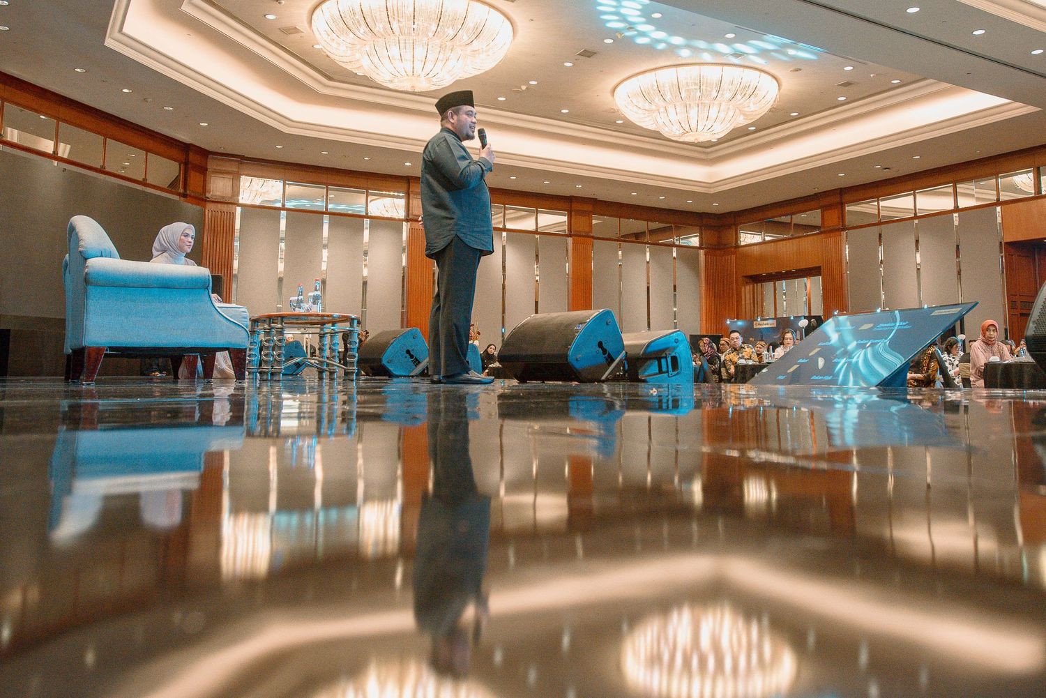A person performs a breakdancing move on a shiny ballroom floor beneath elegant crystal chandeliers.