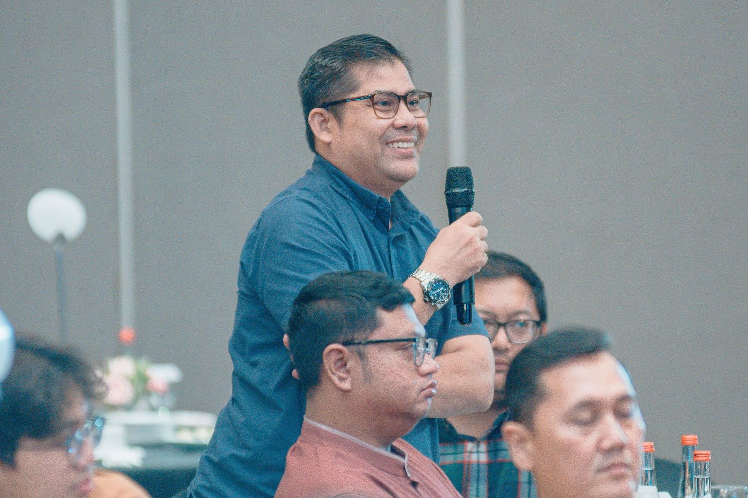 A participant stands and speaks into a microphone during a business conference or meeting.