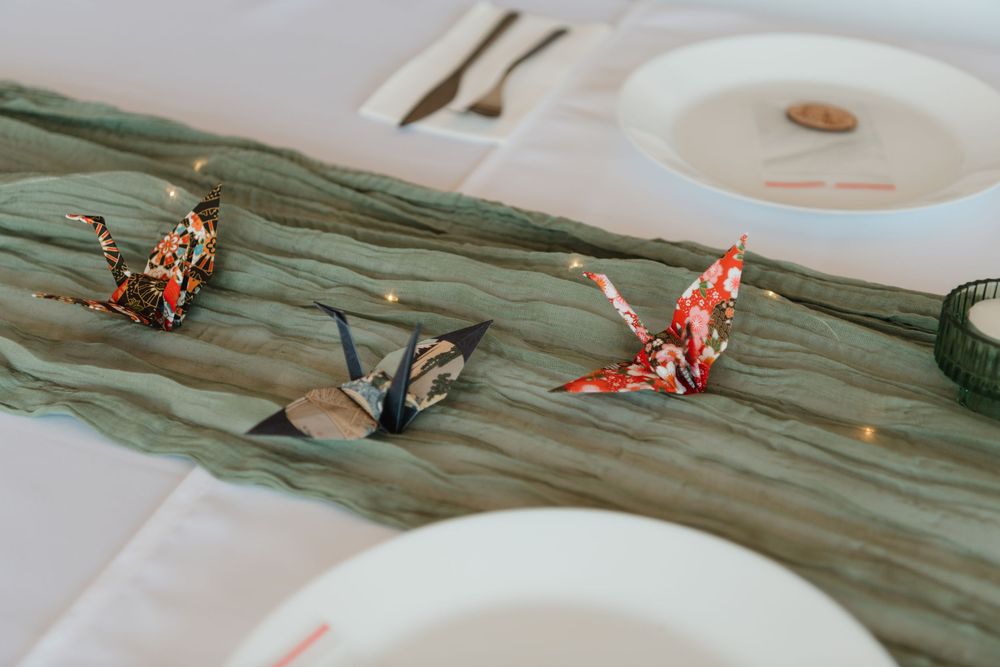 Colorful origami paper cranes displayed on a green fabric table runner at an elegant wedding reception.