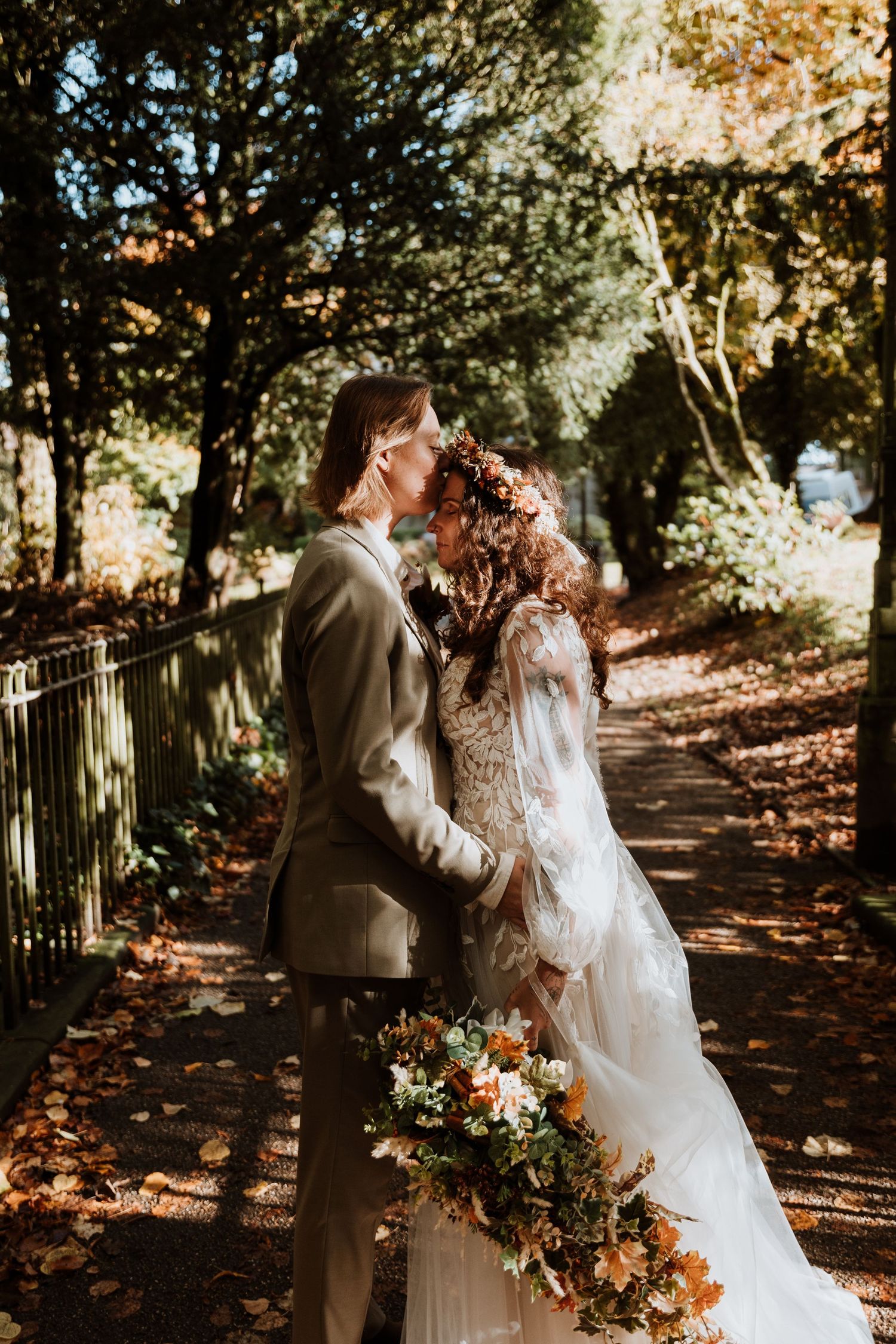 A romantic autumn wedding photoshoot in a wooded path with sunlight filtering through golden leaves.