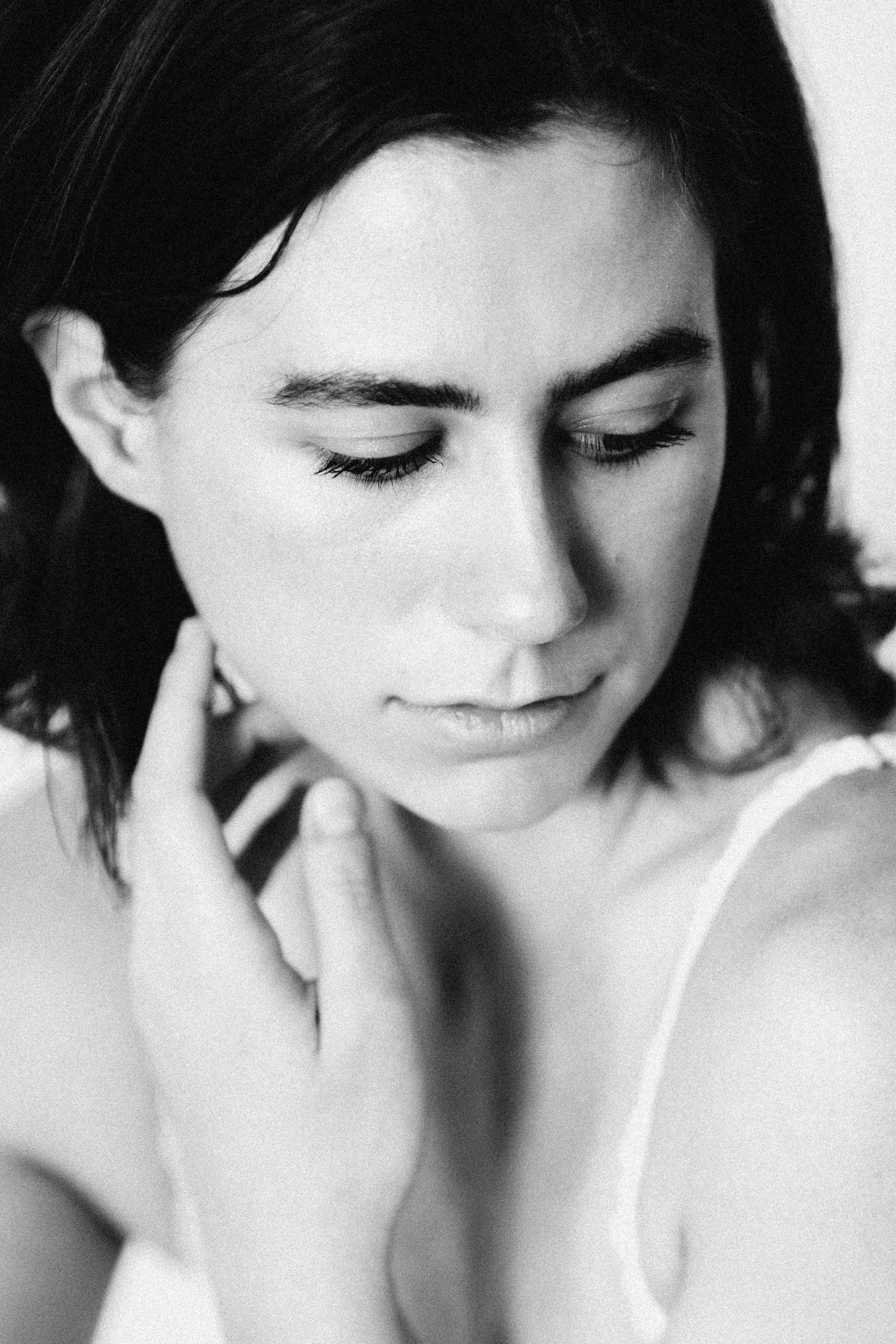 Black and white close-up portrait of a dark-haired woman with closed eyes touching her neck gently.