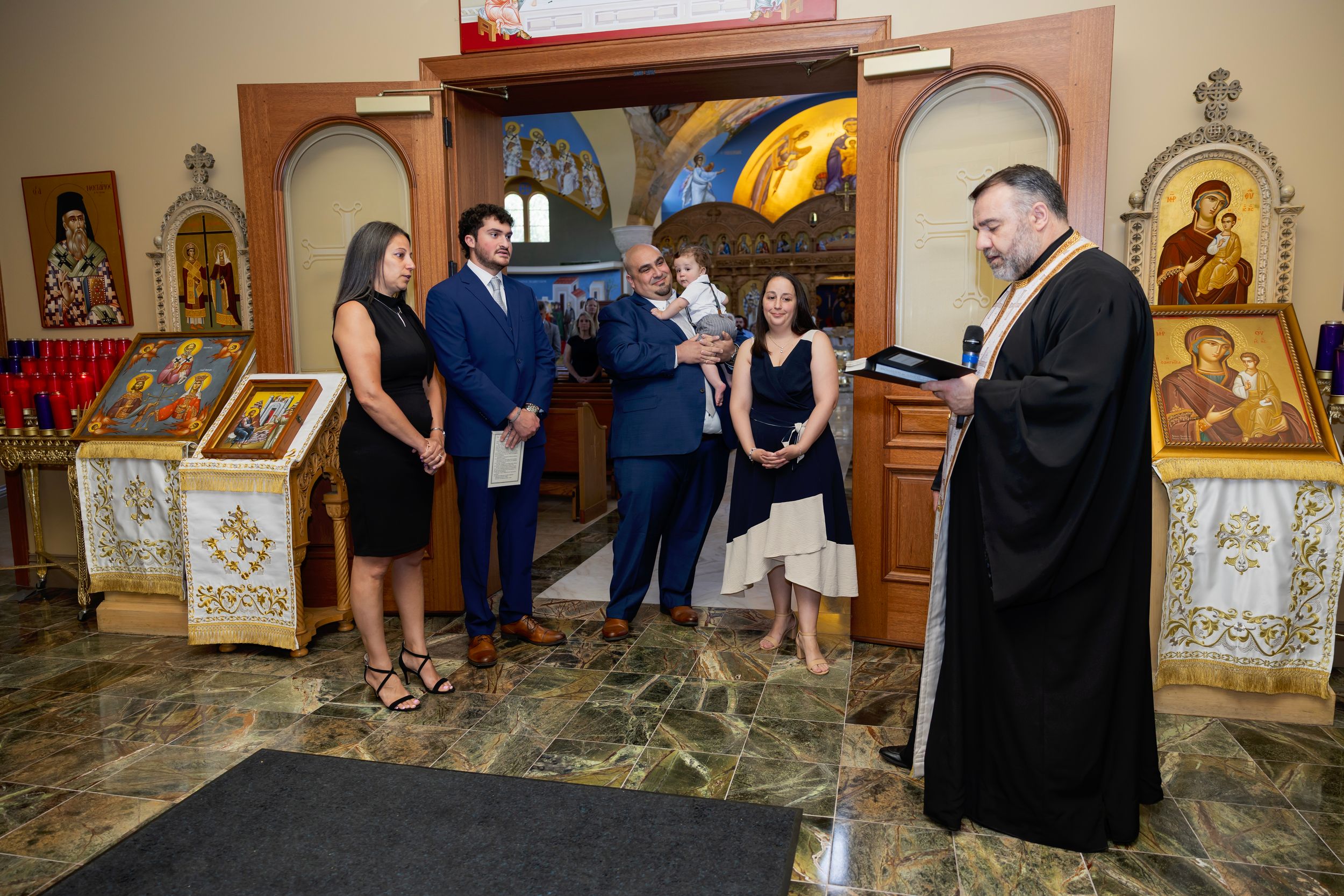 A group gathers inside an Orthodox church with religious icons and decorative arches visible in the background.