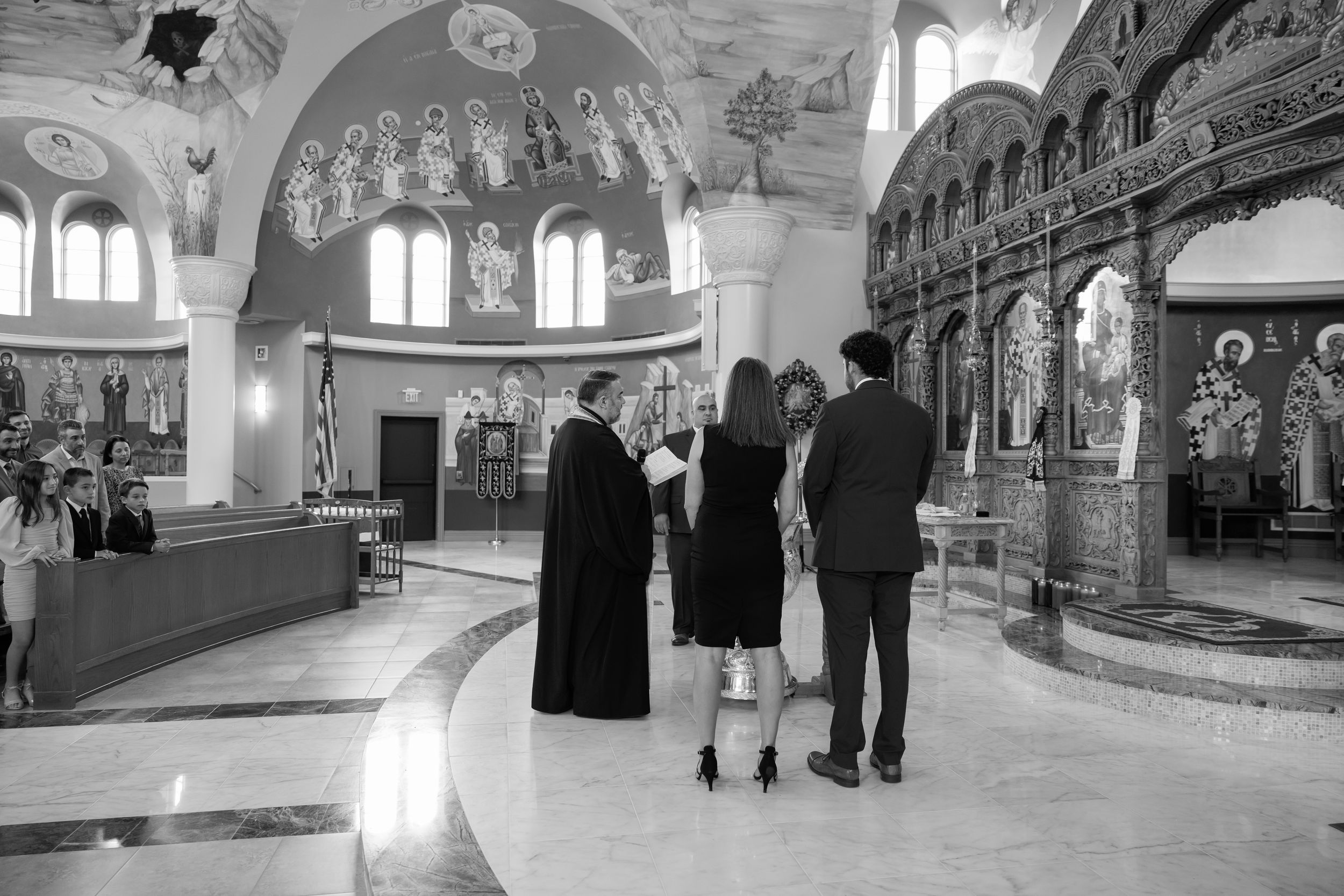 Interior view of an ornate orthodox church with visitors admiring the religious artwork and architecture.