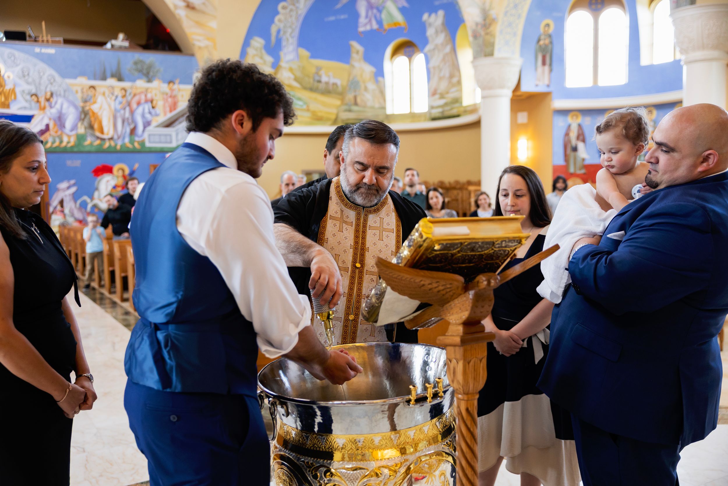 People celebrate in a church with colorful murals and arched windows during a joyous ceremony.