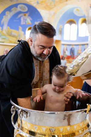 A religious baptism ritual being performed in a church with golden decorative elements and painted murals.
