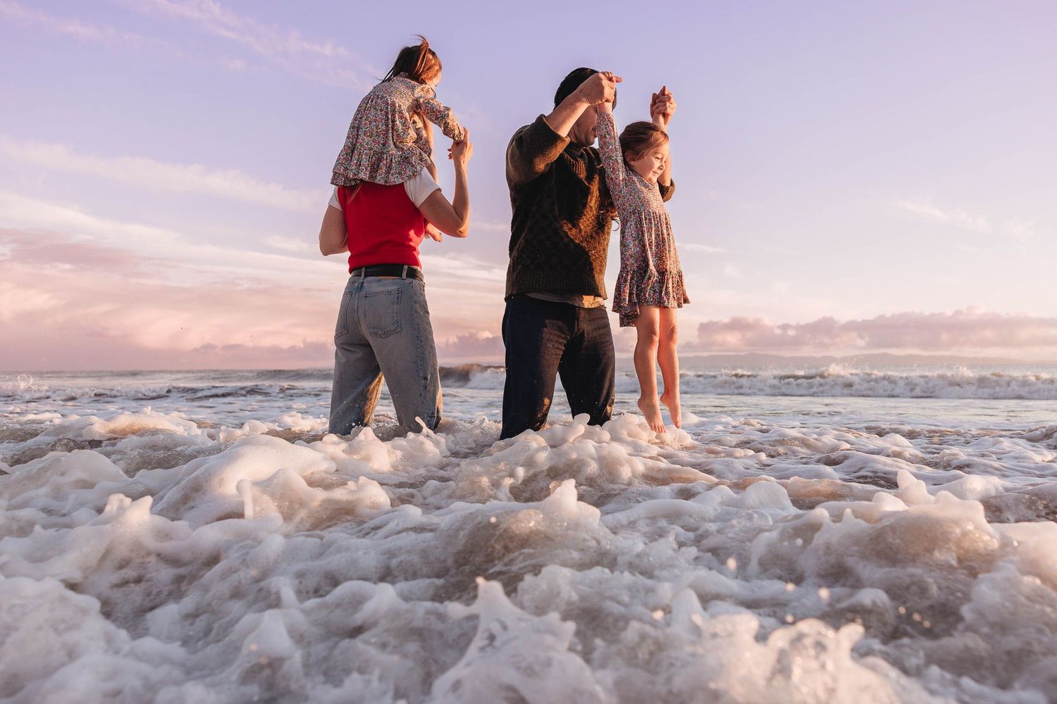 A group of people enjoy playing in the ocean waves at sunset, splashing and wading in the foamy water.