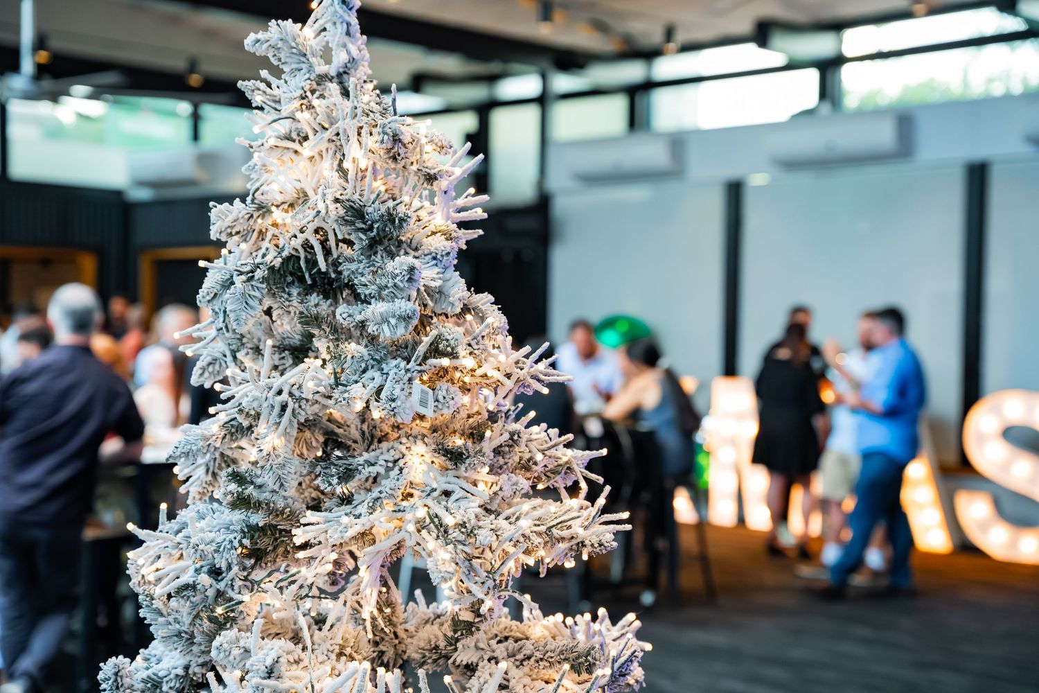 A white Christmas tree decorated with silver ornaments glows in a modern office space.