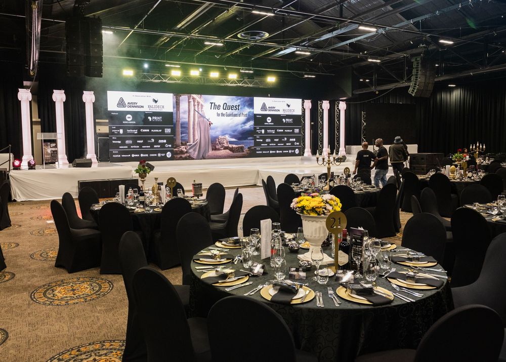 Elegant banquet hall setup with round tables and black chairs arranged for a formal event in a dimly lit venue.