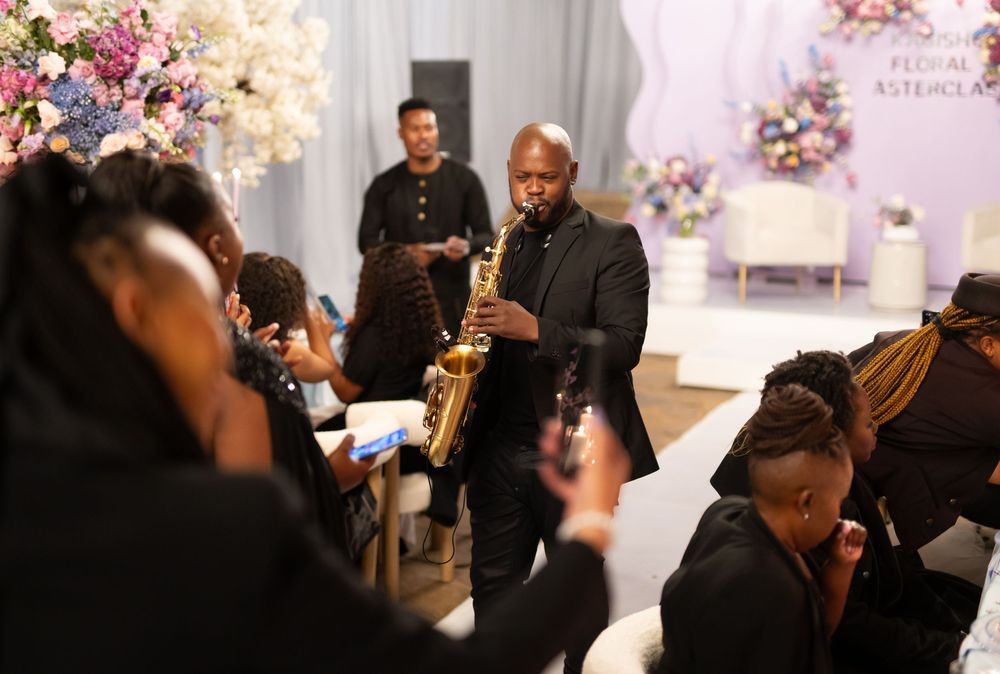 Musicians perform jazz music with saxophone and instruments at an elegant indoor event with floral decorations.