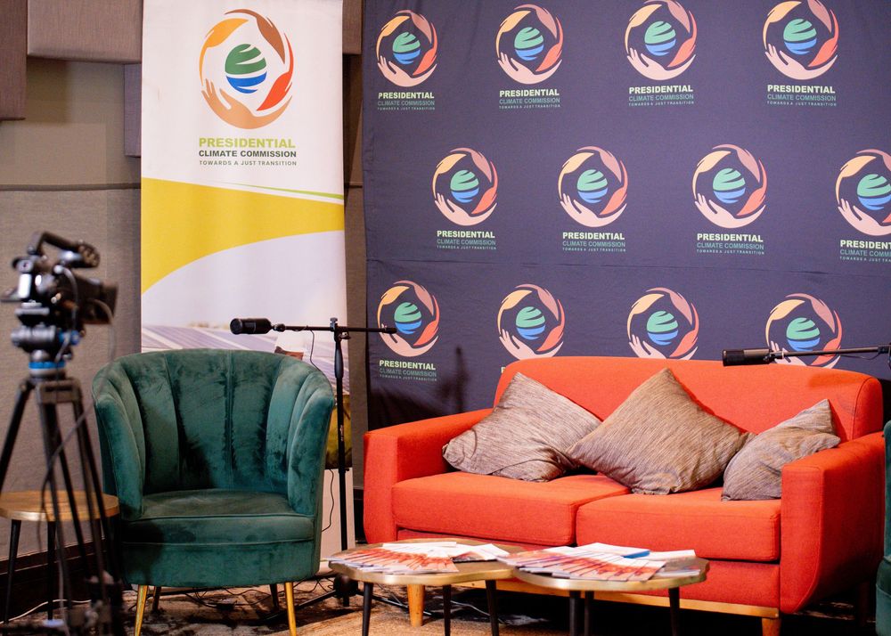 Modern living room setup featuring colorful sofas in orange and teal with branded wall displays and camera equipment.