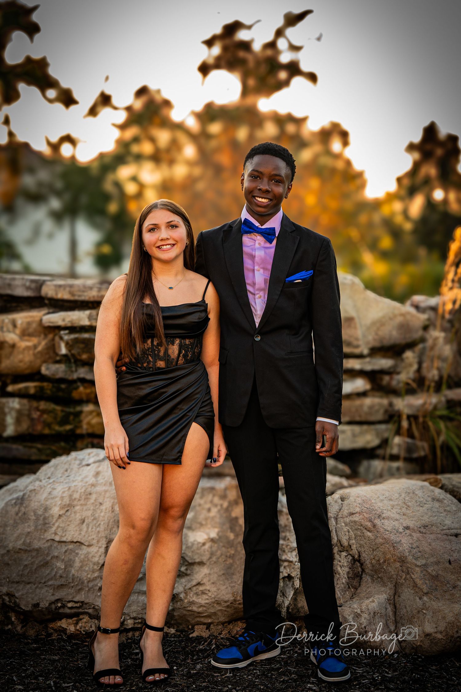 Couple in formal wear posing on rocky terrain during golden hour.