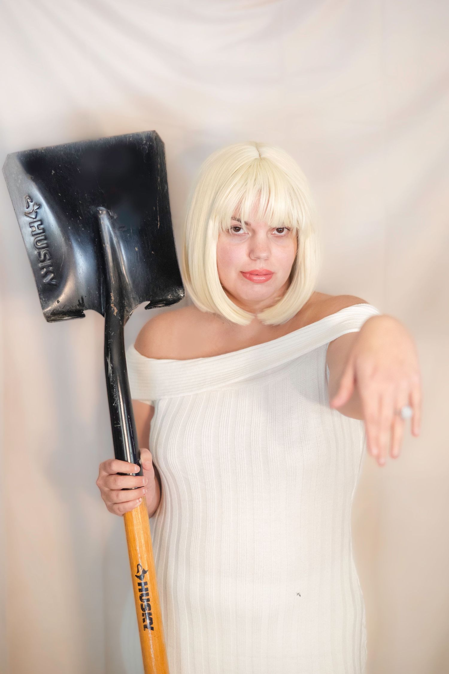 woman in a white dress poses with a large black shovel cosplays as Debbie from Addams Family Values Halloween Costume Photoshoot