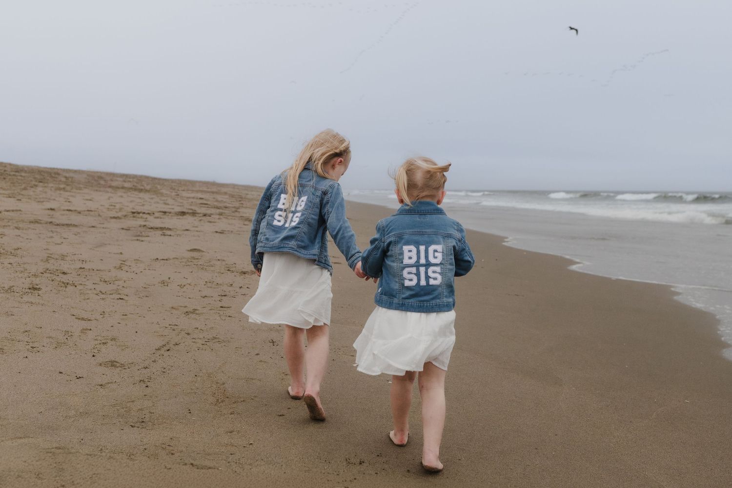Two people walk along a misty beach shoreline on an overcast day with waves rolling in from the ocean.