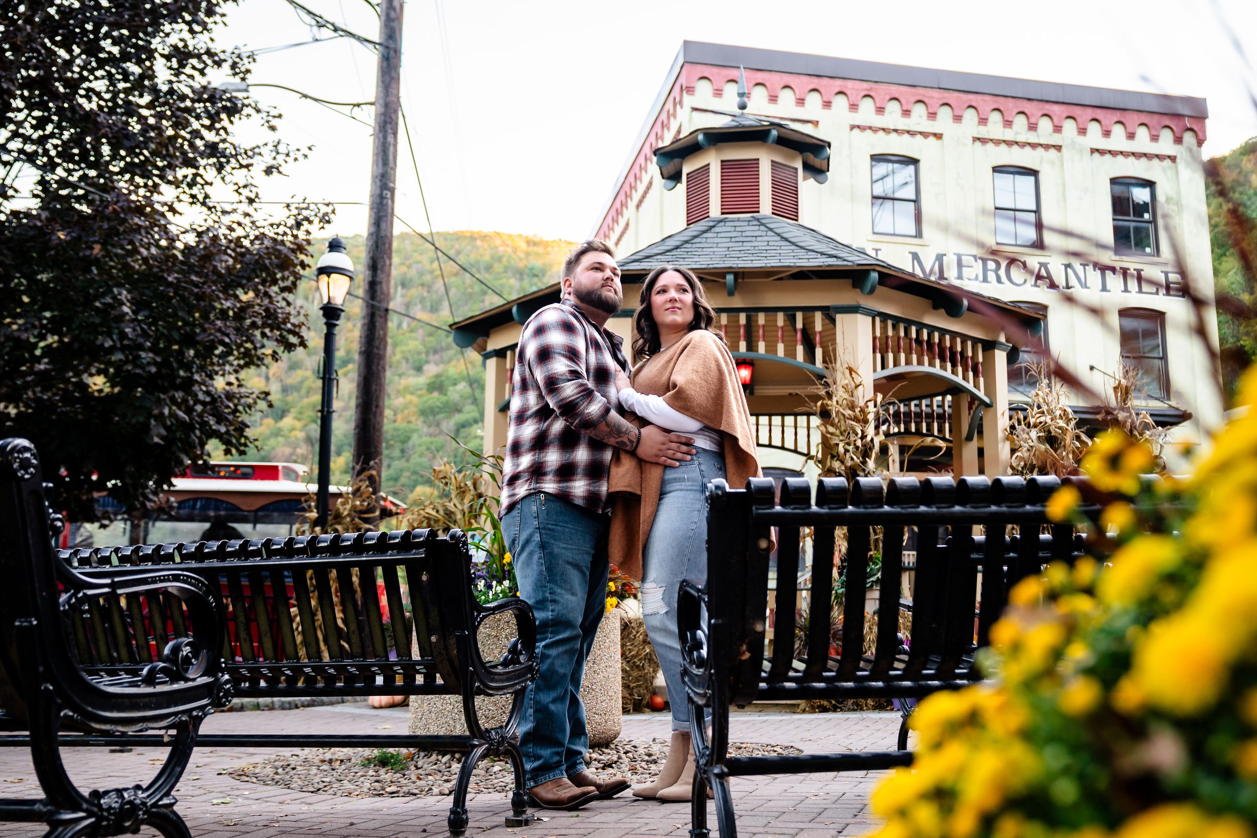 Couple enjoying fall day together near decorative wooden railings and yellow flowers.