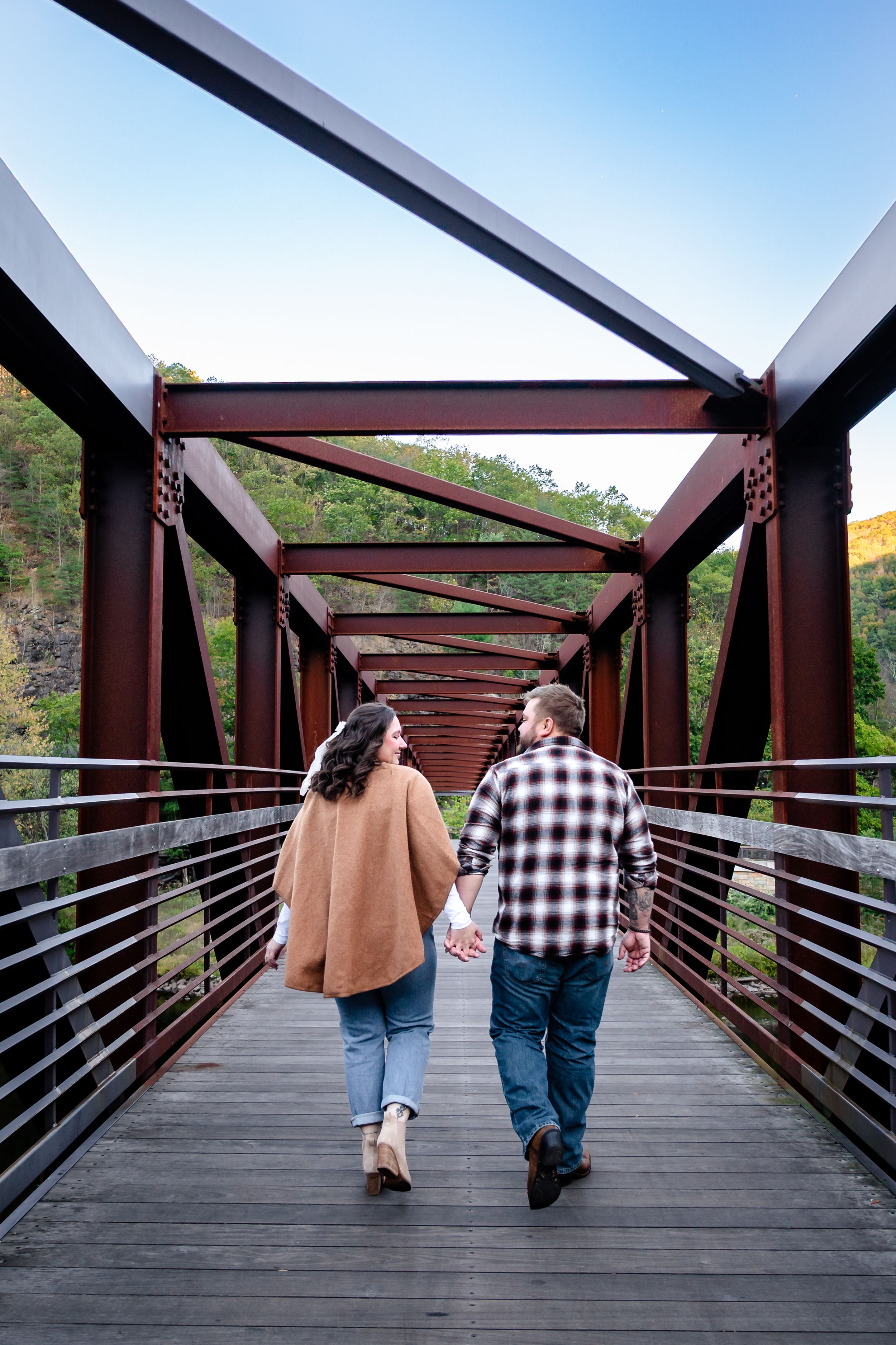 Couple walking hand in hand across modern metal and wood bridge structure.