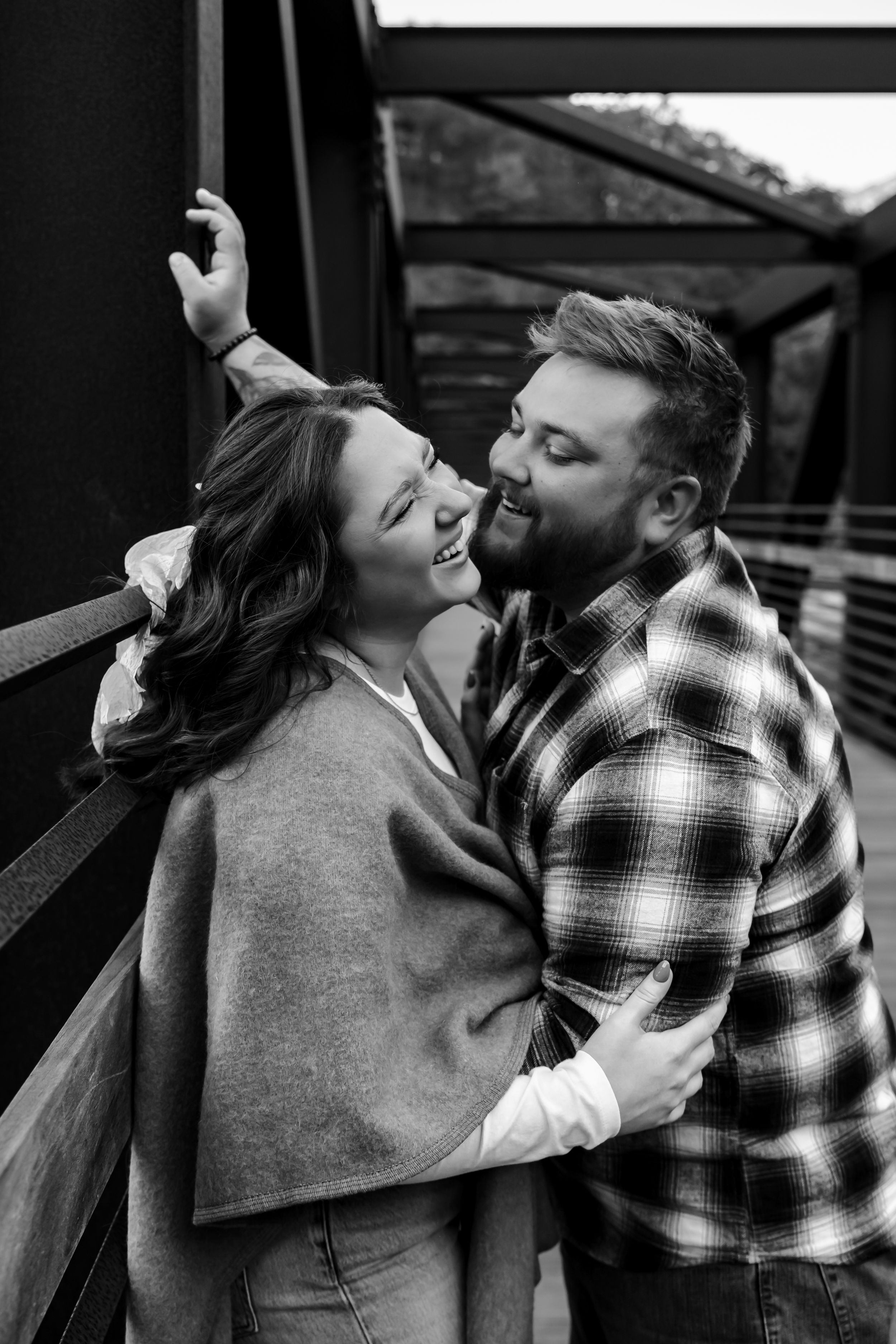 Romantic black and white photo of couple sharing tender moment on bridge.
