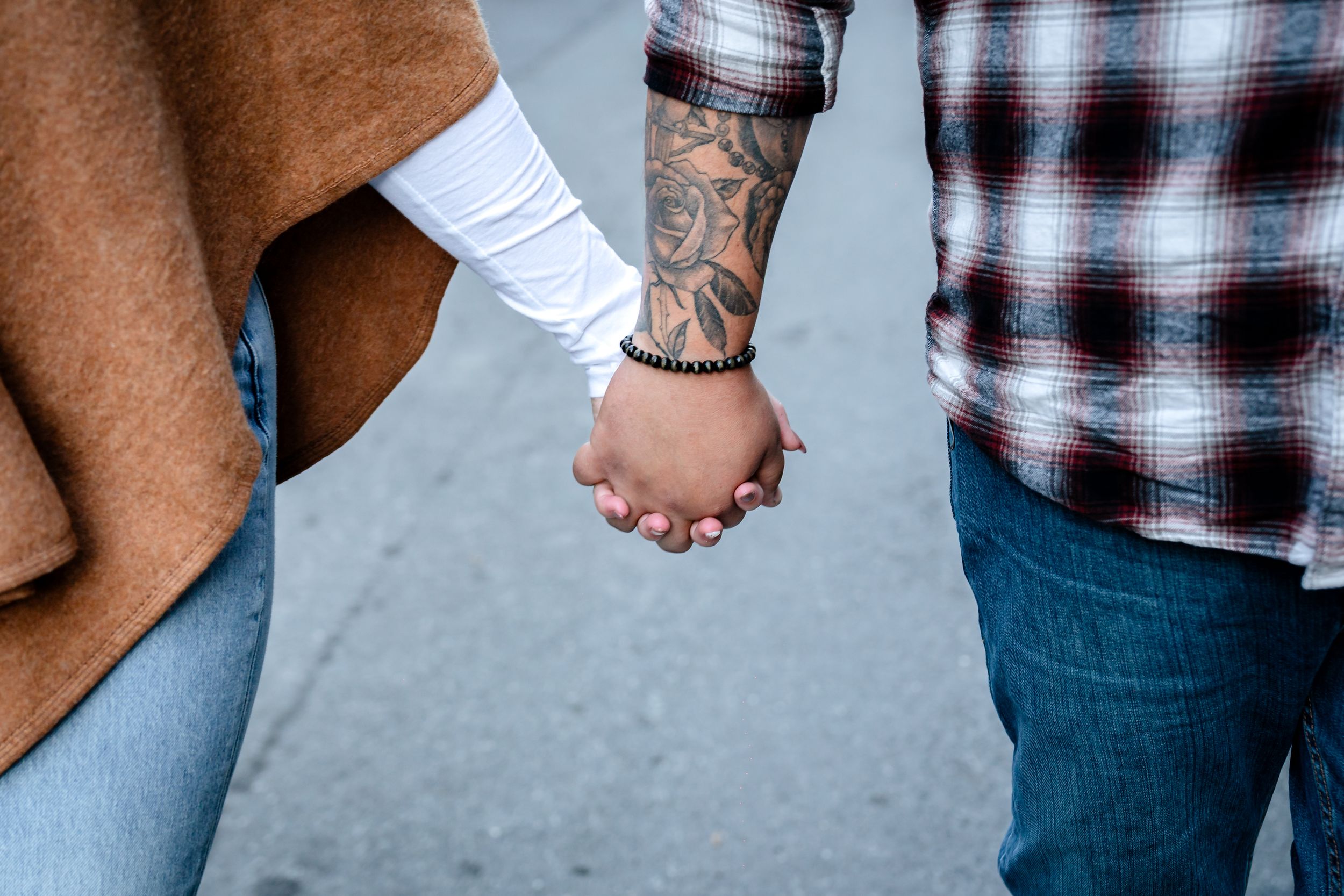 Close-up of couple holding hands wearing plaid shirt and brown coat.