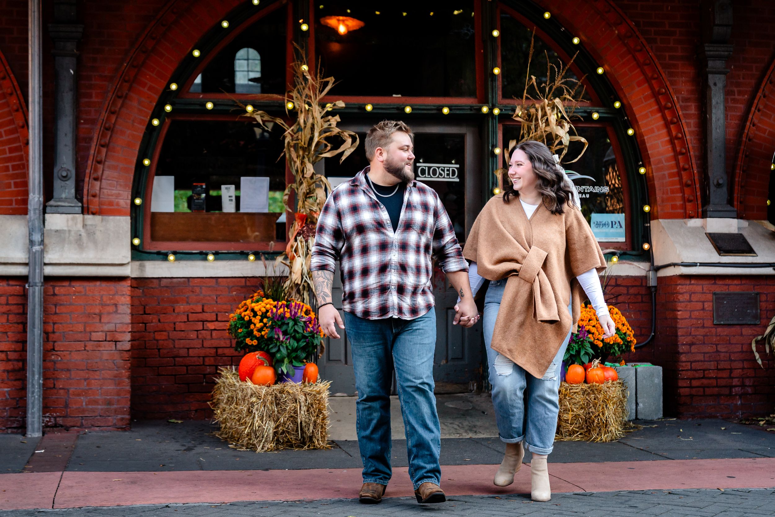 Couple sharing romantic moment outside brick building with autumn decorations.