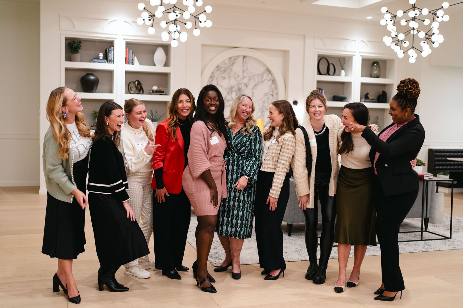 Group of women in professional attire posing together in an elegant white room with built-in shelving.