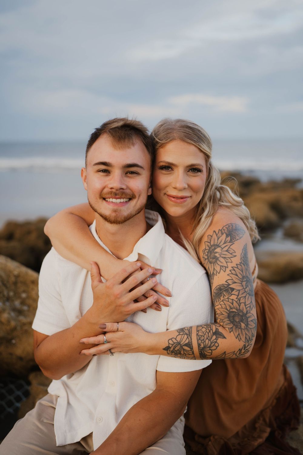 A couple embraces outdoors during a sunset photoshoot near a lake with natural scenery in the background.