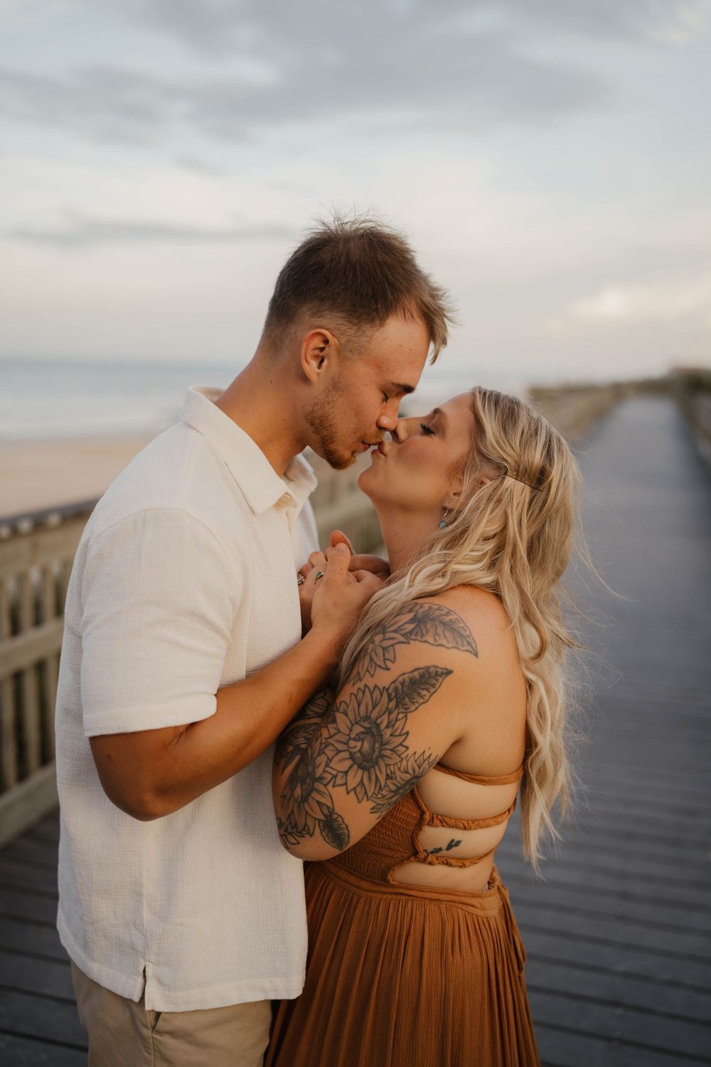 Romantic couple shares intimate moment on wooden boardwalk during sunset photoshoot.