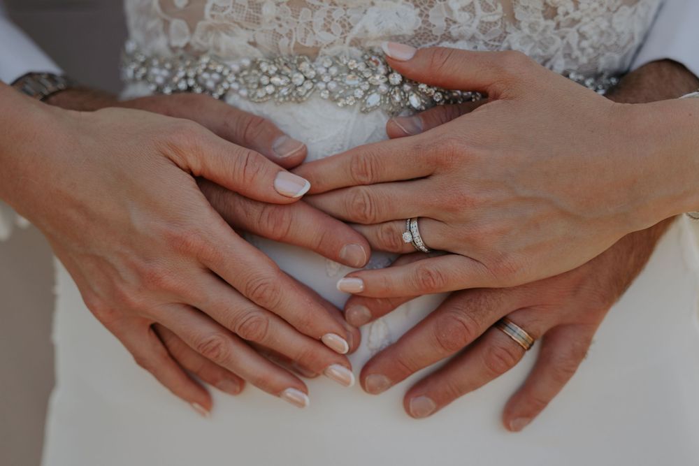 Close-up of bride and groom's hands showing wedding rings resting on bridal gown.