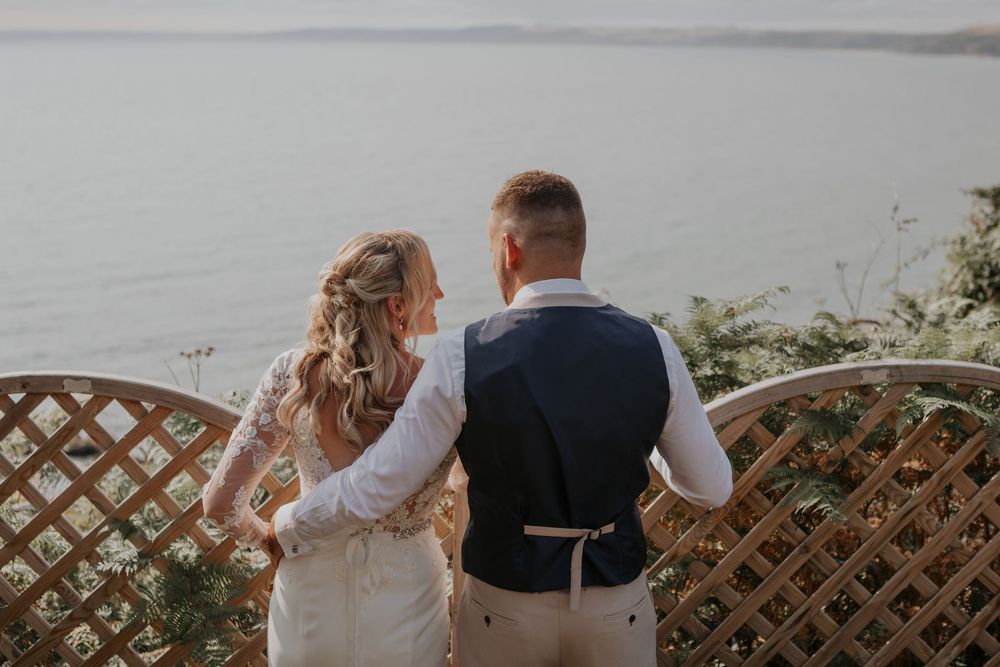 Bride and groom standing together overlooking a serene ocean view at their outdoor wedding venue.