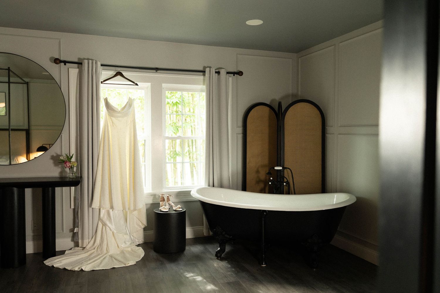 Elegant black clawfoot bathtub sits in a bright bathroom with white walls and natural light streaming through windows.