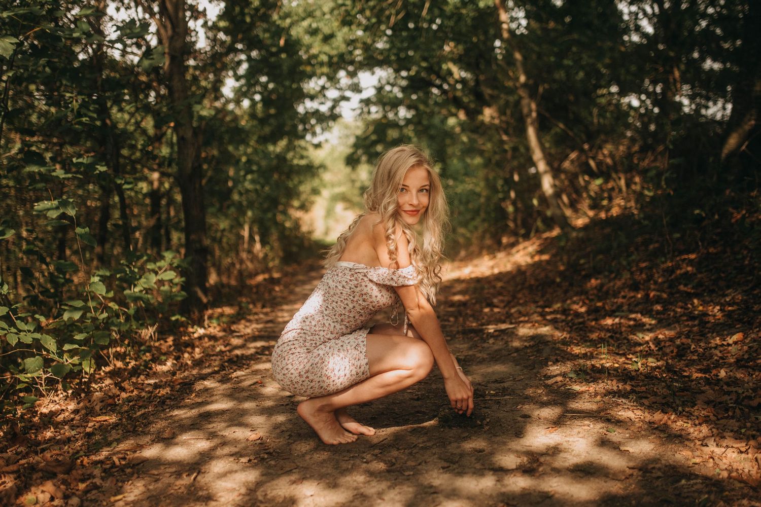 Sunlit forest portrait session with dappled light filtering through autumn trees.