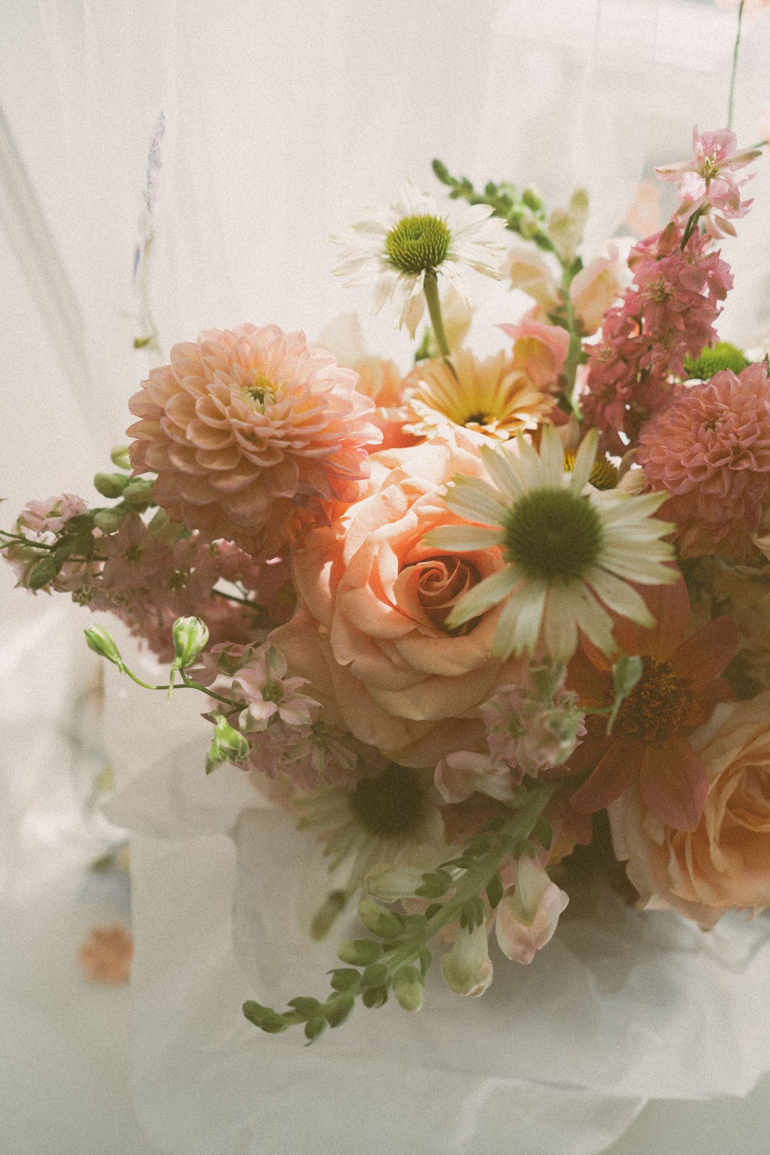 Soft peach roses and white daisies arranged in a romantic bouquet with pink florals against a light background.