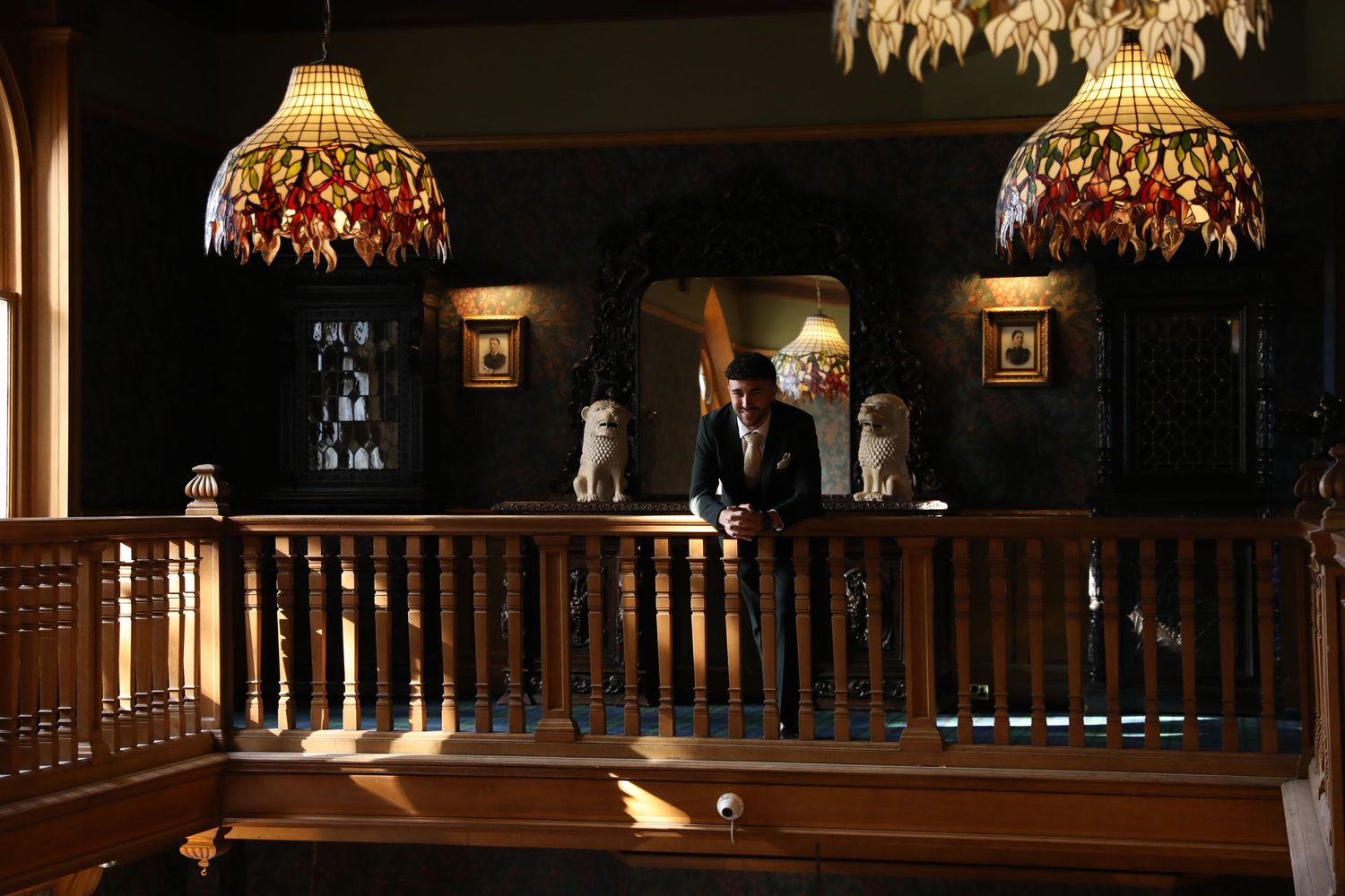 Elegant Tiffany-style pendant lamps illuminate a dark wood balcony railing in a vintage interior setting.