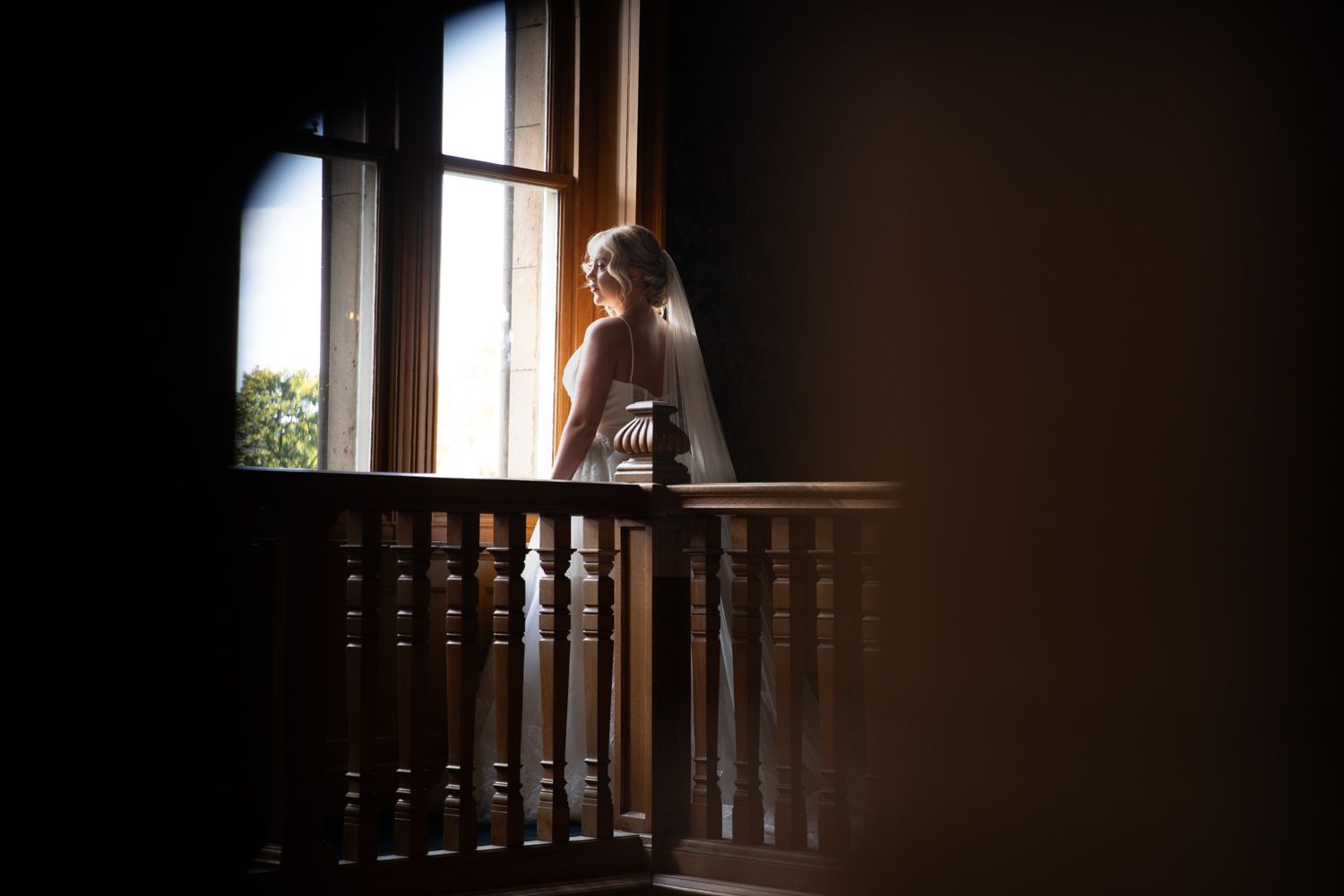 A silhouetted figure stands by a window in a dark room with dramatic lighting creating a moody atmosphere.