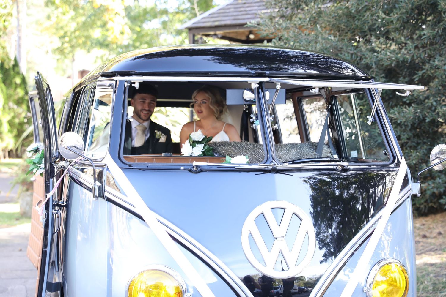 Classic blue and white Volkswagen bus with roof rack parked on a sunny day with occupants inside.