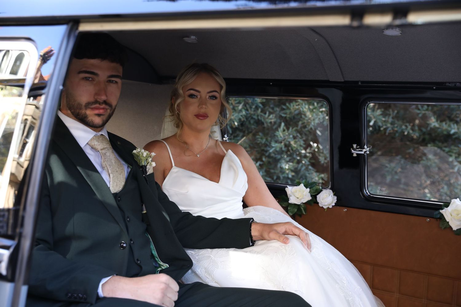 A couple sits in a vintage car during their wedding celebration, with the bride wearing a white dress and veil.