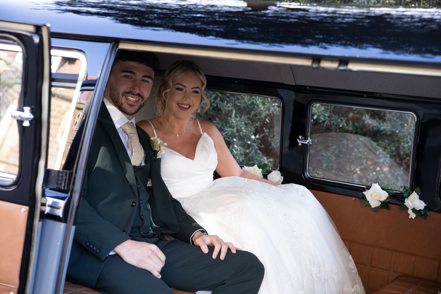 A couple shares a romantic moment in the backseat of a vintage car on their wedding day.