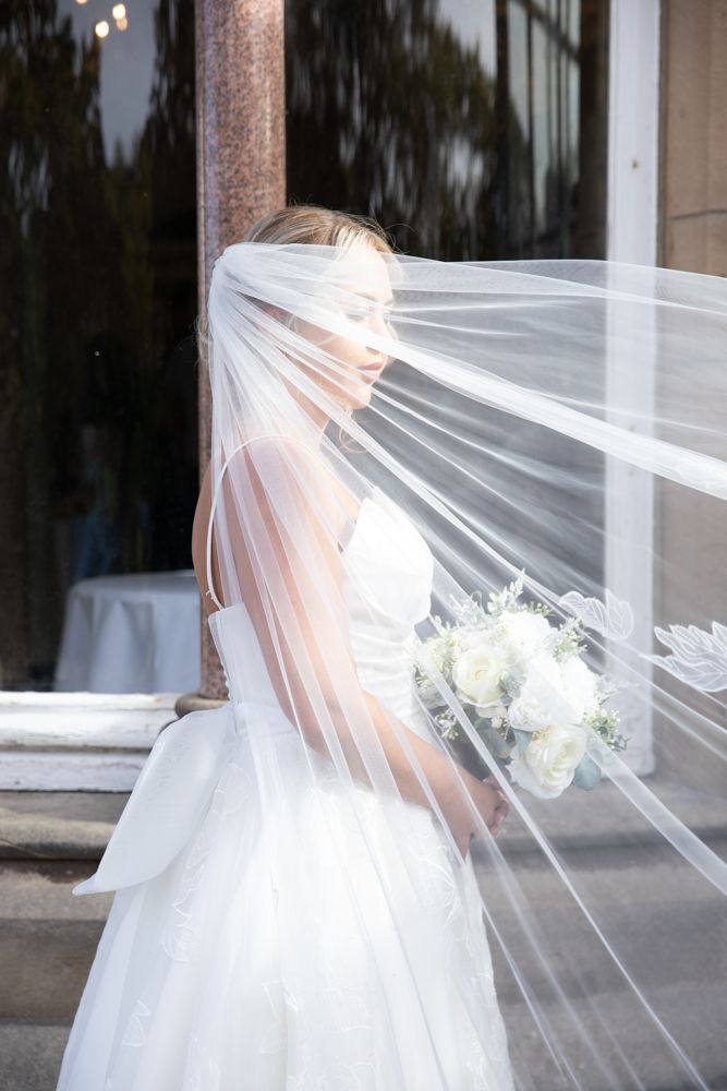 A flowing white wedding veil catches the breeze in a series of artistic bridal portraits against a light background.