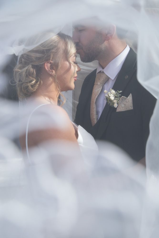 Romantic wedding moment captured through soft veil creating dreamy effect in natural light.