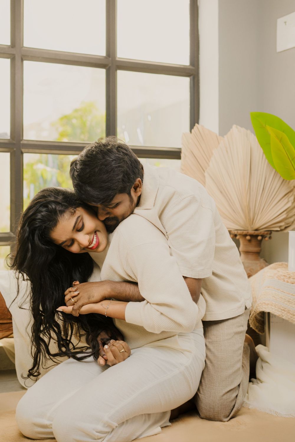 A romantic couple in white outfits poses artistically with decorative fans in a bright indoor setting.