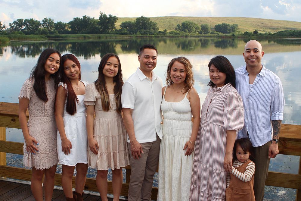Family gathering on lakeside deck wearing coordinated white and neutral summer outfits.