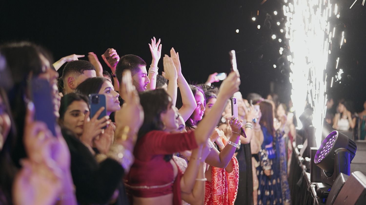 Excited crowd celebrates at a concert with sparklers and colorful lighting effects.