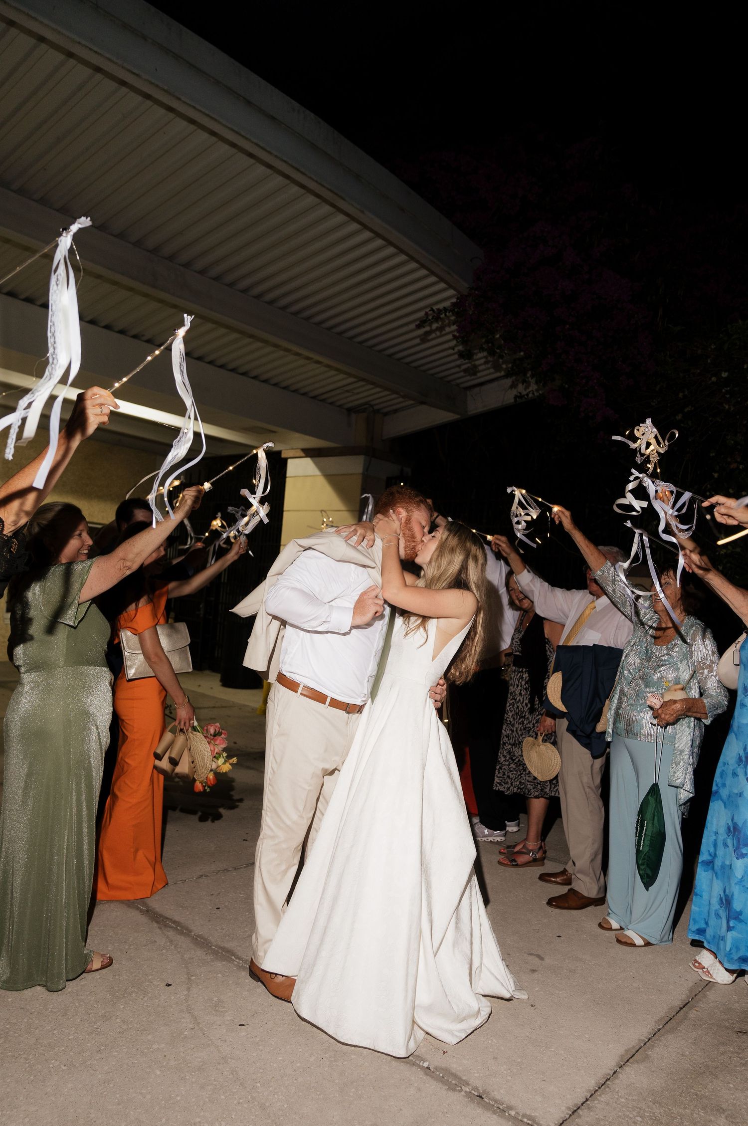 Wedding guests dance and celebrate while holding sparklers during an evening outdoor reception celebration.