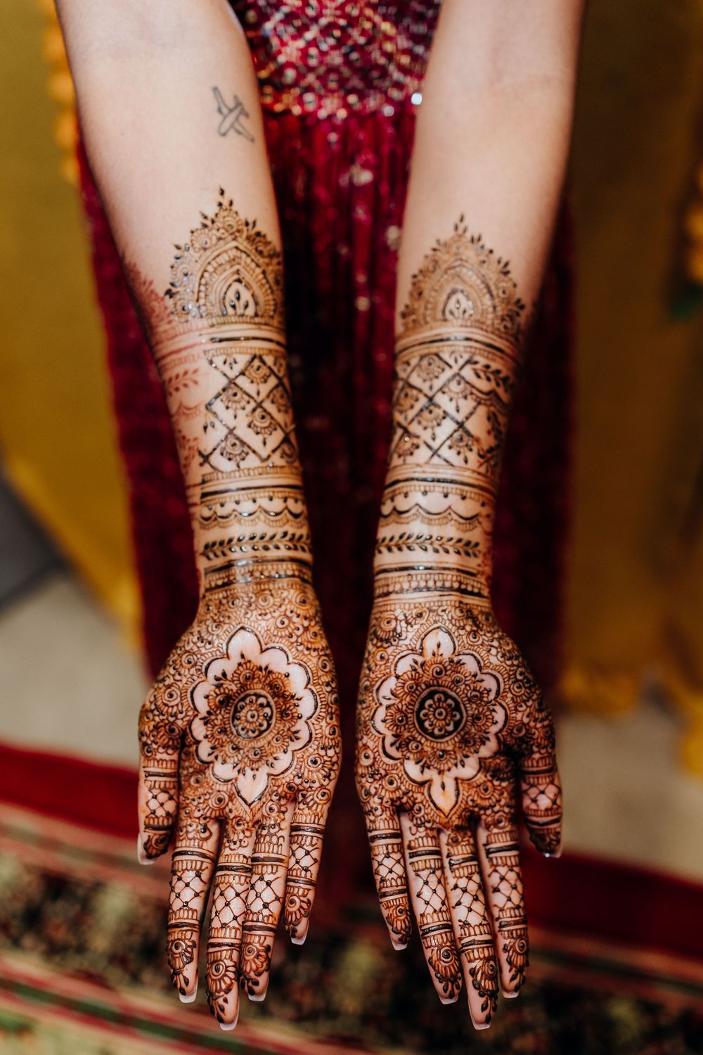 Intricate henna mehndi designs displayed on both hands against red fabric background.