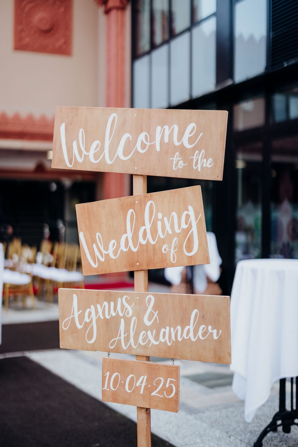 Rustic wooden wedding welcome signs with white calligraphy displayed at an outdoor venue.