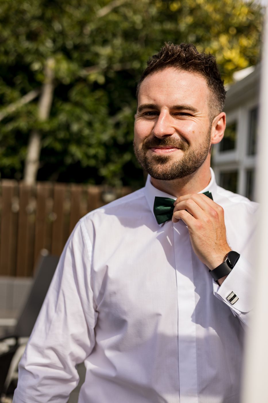 Person in white dress shirt smiling while adjusting formal attire outdoors.