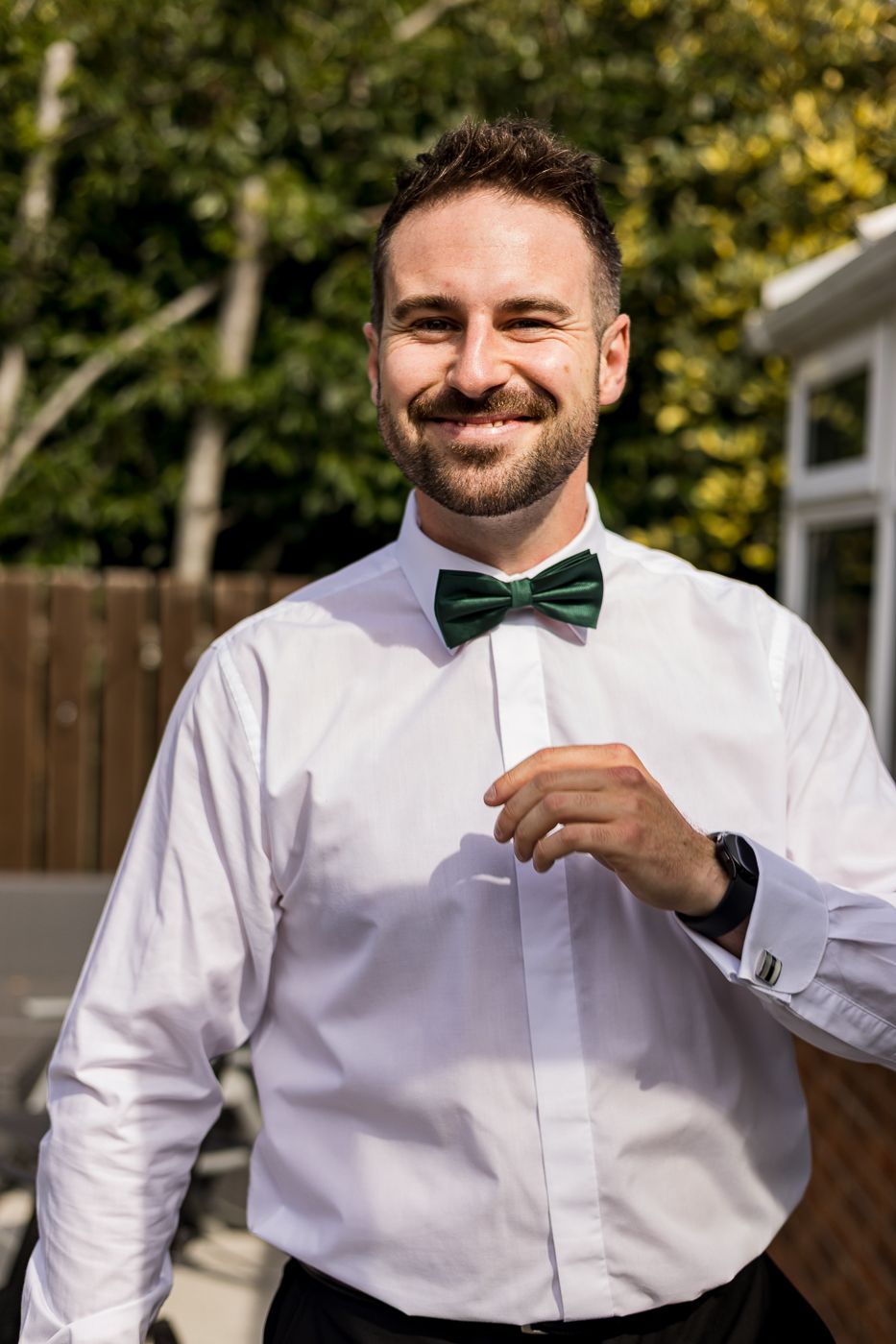 Man in white dress shirt and green bowtie smiling during outdoor formal event.