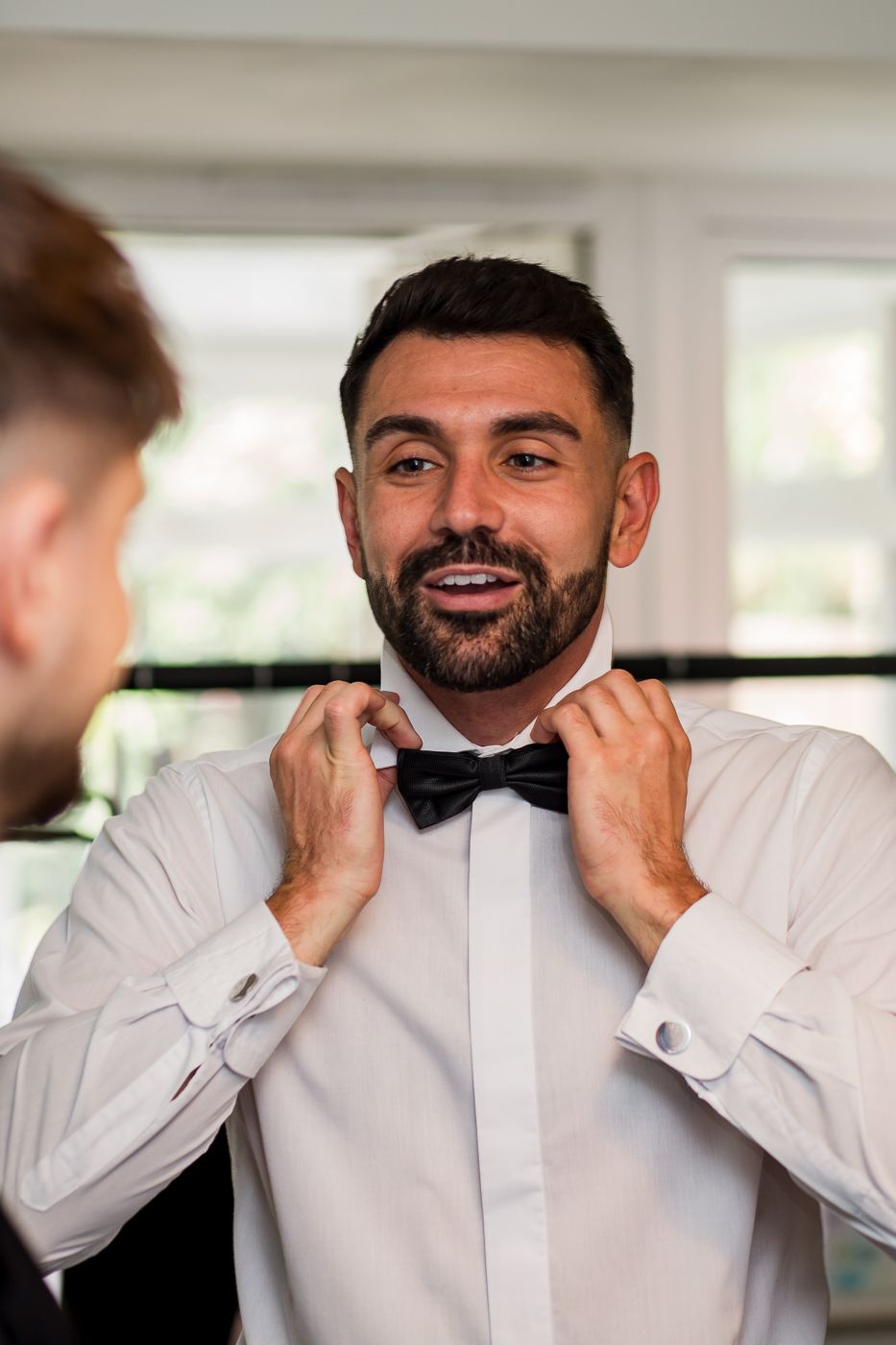 Groomsman adjusts black bow tie while wearing crisp white dress shirt.