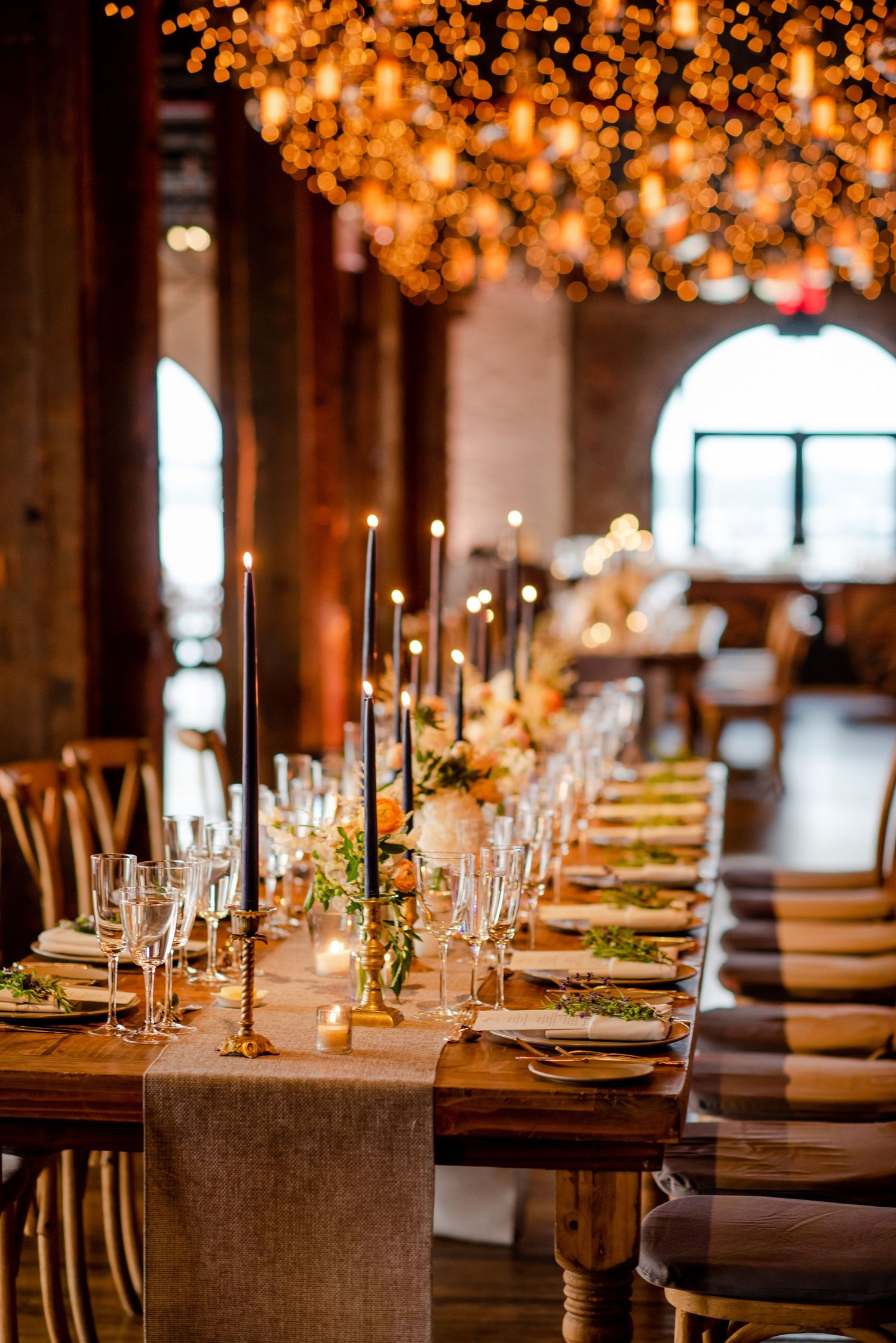 Elegant wedding reception tables set with candles, glassware and warm overhead lighting.